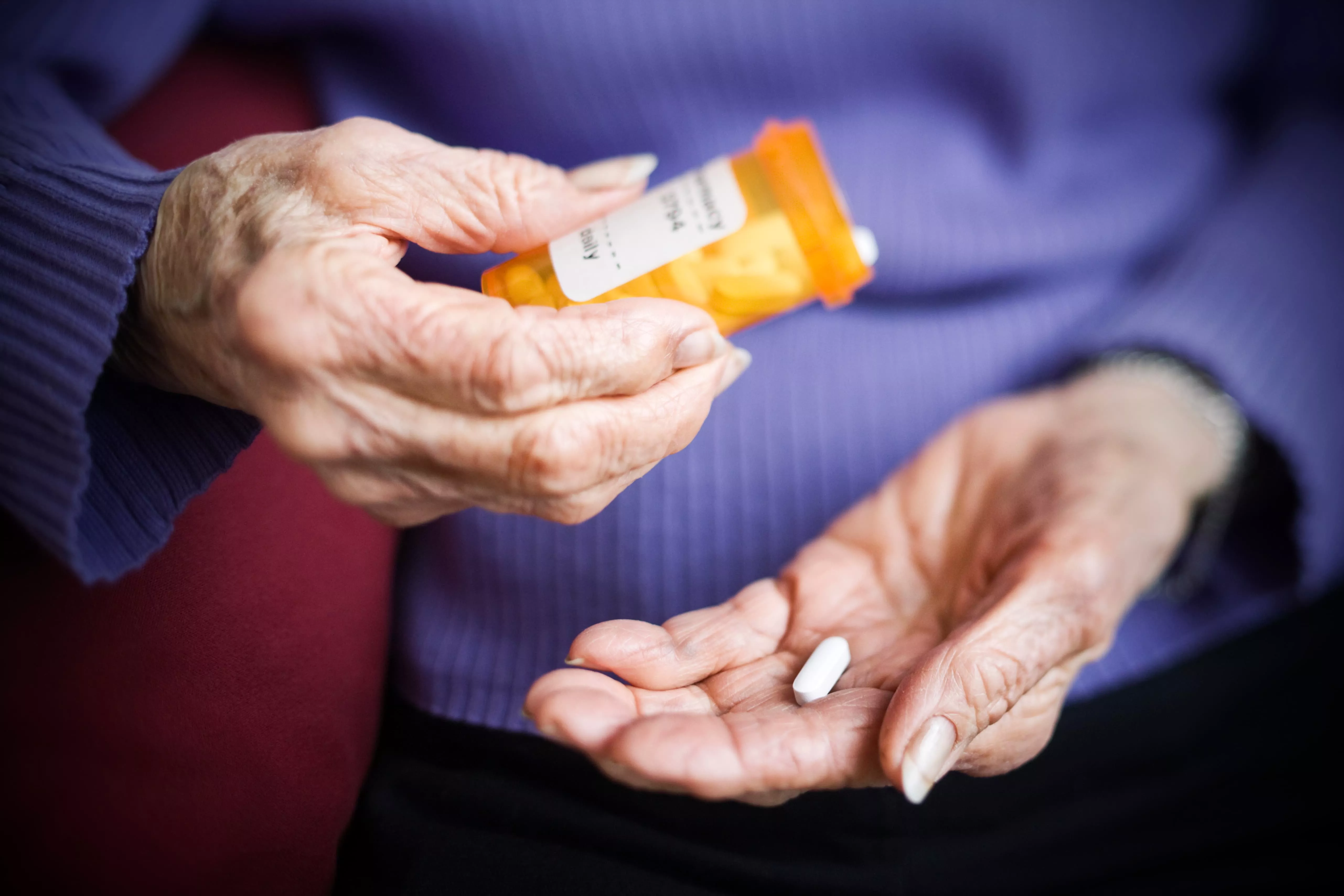 An old person takes a tablet from its container